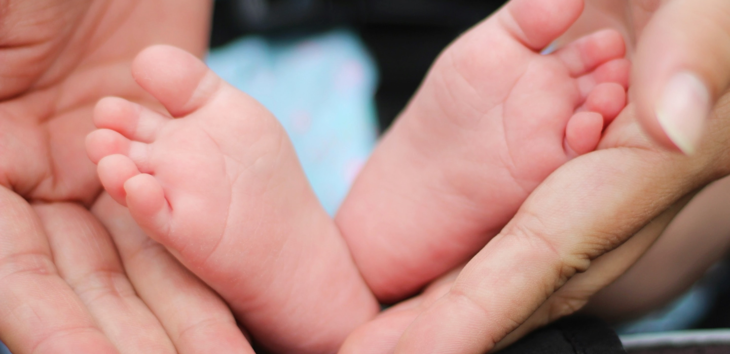 Babyfüße werden vorsichtig von einer Hand gehalten