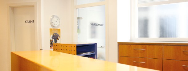 Der Eingangsbereich der Praxis bestehend aus einem Holzcounter und Regalen mit zwei Türen im Hintergrund